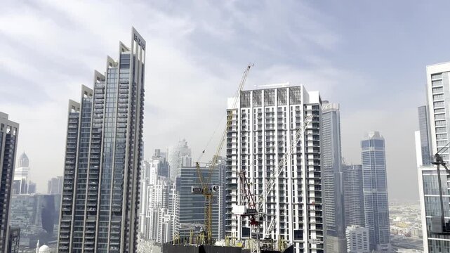 Modern Dubai skyline with luxury high-rise towers, construction cranes and contemporary urban architecture under a hazy blue sky, panoramic cityscape, showing rapid real estate development in the UAE.