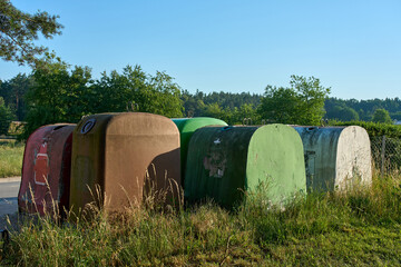 Obraz premium Row of public glass recycling containers in Germany. Colorful dome-shaped waste bins for sorting bottles outdoors near a forest. Concept of ecology, environmental care, and trash management.