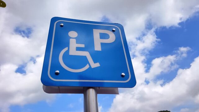 A blue parking sign for disabled people against a sky with clouds