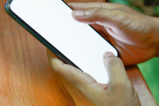 Close up of hands holding a smartphone with blank white screen on wooden table background. Mockup concept.