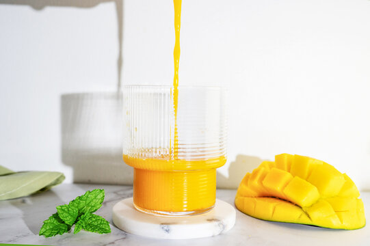 Pouring fresh mango smoothie into a glass on a white table with shadows.
