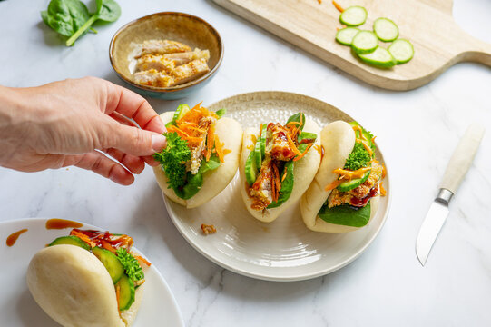 Female hand stuffing steamed bao buns, Asian culinary tradition.