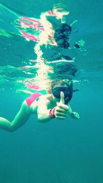Underwater view of a female snorkeler giving a thumbs up gesture. Woman swimming and snorkeling in the turquoise sea of Puerto Morelos, Mexico.
