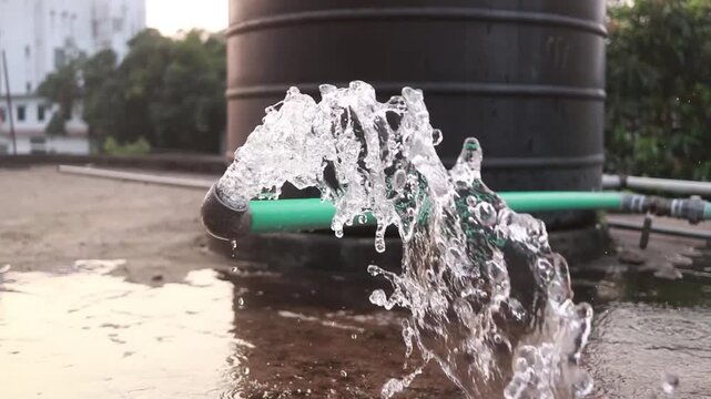 Clear water flows with great force from a green plastic pipe located on a rooftop while creating a lively splash against the ground in this high quality video footage capture of a refreshing stream du