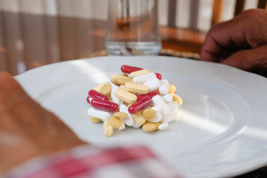 Person's hands near white plate overloaded with capsules and pills, needing medication