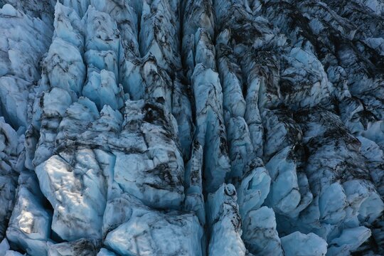 Aerial view of the crevassed surface of Falljokull glacier with deep blue ice and dark volcanic ash deposits in Svinafell, Sveitarfelagid Hornafjordur, Iceland.