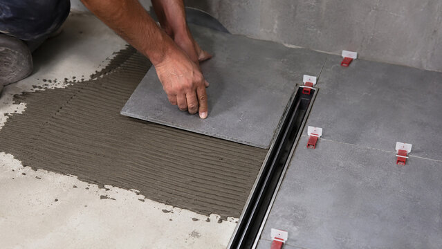 Professional worker laying large grey floor tile in bathroom