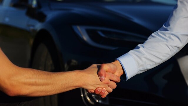 Male hand giving key of car to buyer of electric automobile outdoor. Handshake between salesman and new owner of modern auto after successful deal. Concept of buy or rent car. Slow mo