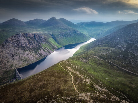 Aerial view of Ben Crom Reservoir nestled among rugged Mourne Mountains with green slopes, rocky terrain, and calm water in Newry, Northern Ireland, United Kingdom.
