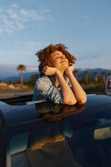 Fototapeta premium A woman enjoys a sunny day, leaning from car windows with a relaxed smile, embodying casual lifestyle and outdoor freedom, capturing a carefree travel vibe against a blue sky.