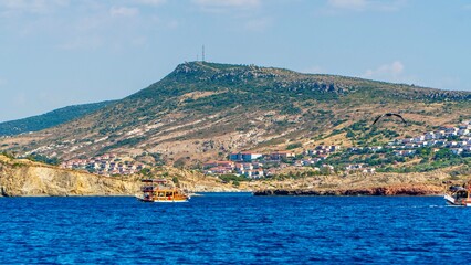 Fototapeta premium Izmir, Turkey - June 21, 2026: Scenic nature view near Foça, featuring Mediterranean vegetation, rocky coastline, green hills, blue Aegean Sea, calm water, and natural coastal landscape.