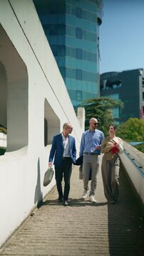 A team of business professionals walks through a modern urban landscape, engaged in discussion. This scene captures colleagues moving purposefully outdoors amidst contemporary architecture.
