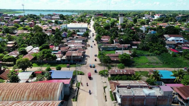 Aerial drone video tracking a busy unpaved street in Yarinacocha, Pucallpa, featuring motorcycles and mototaxis in a rustic tropical town setting.