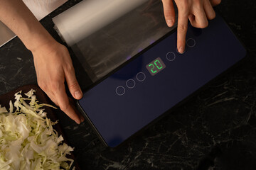 Hand setting vacuum sealer for packing shredded cabbage at home kitchen. © Anastassiya 