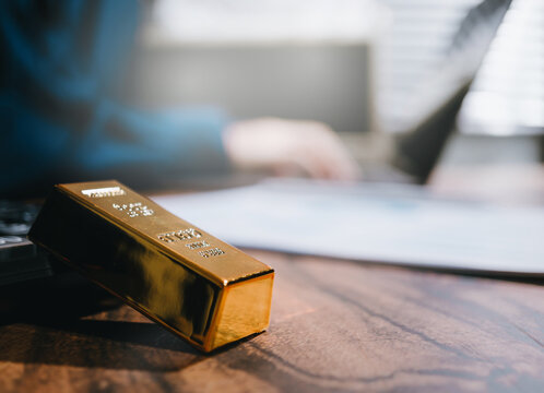 Gold investment concept. Gold bar on office desk with financial report for wealth management, asset protection, market analysis, and economic security.