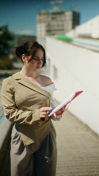A young businesswoman or student writes diligently in a bright red notebook outdoors. She is focused on her tasks, taking notes or planning in an urban setting.