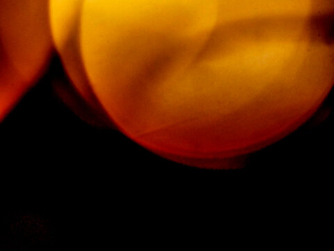Abstract bokeh background with warm orange and yellow light circles on black. Blurred glowing orbs create soft, dreamy visual effect. Light leaks for design and special effects.