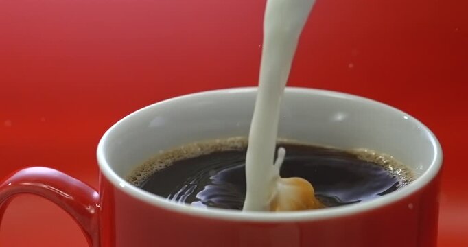 Cream pouring into coffee in a red mug super slow motion