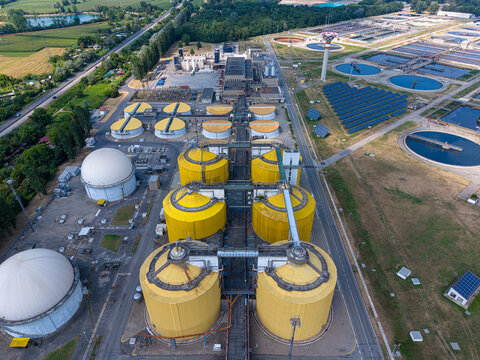 Aerial view of the wastewater treatment plant featuring large yellow digester tanks, white storage domes, and circular sedimentation basins in Settimo Torinese, Piedmont, Italy.