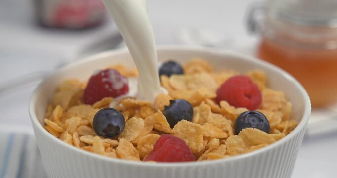 Milk pouring with splash into cornflakes with berry breakfast cereal bowl healthy morning meal