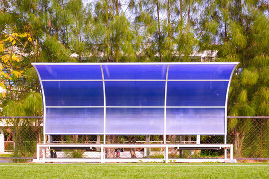 Team bench dugout on green artificial turf soccer field with a background of pine trees in public park. Front view