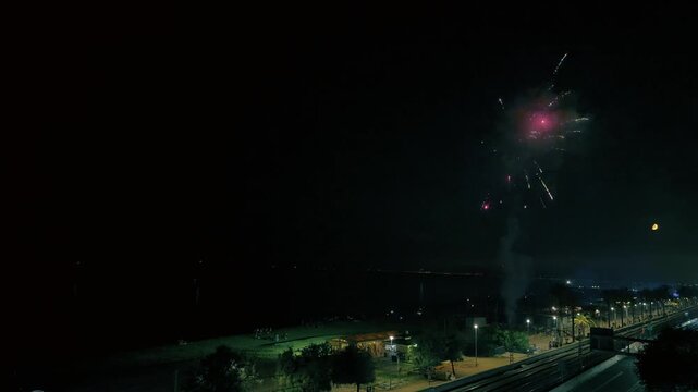 V&iacute;deo 4K nocturno de fuegos artificiales durante una fiesta mayor, con explosiones de luz en el cielo sobre un entorno urbano costero. La escena transmite ambiente festivo, celebraci&oacute;n popular y ocio 