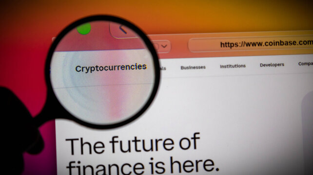 Closeup of a magnifying glass over the coinbase website homepage on a computer screen