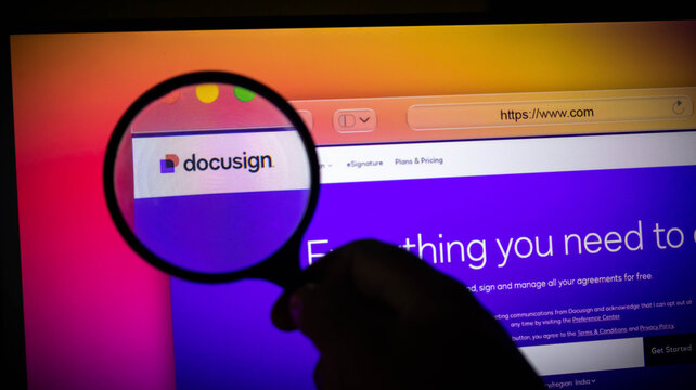 Closeup of a hand holding a magnifying glass over a computer screen showing the docusign website