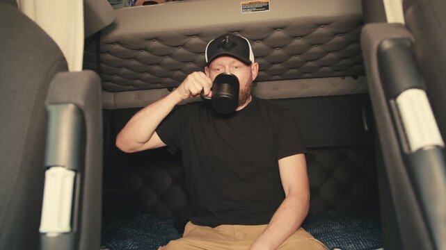 Professional truck driver drinking coffee in sleeper cabin
