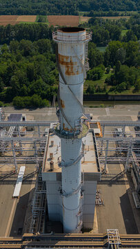 Aerial view of a tall industrial chimney with a spiral staircase and visible rust stains at a power plant facility in Chivasso, Piedmont, Italy.