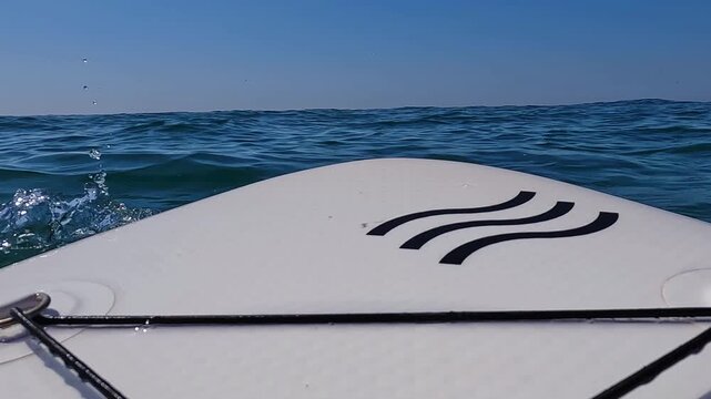 V&iacute;deo de paddle surf grabado desde una perspectiva subjetiva, con la parte delantera de la tabla en primer plano avanzando sobre el mar. Se aprecian olas suaves, horizonte abierto y luz natural, trans