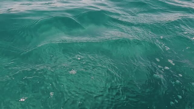 V&iacute;deo 4K de la superficie del mar en primer plano, con agua turquesa, peque&ntilde;as olas, ondulaciones y remolinos suaves. Imagen abstracta y natural del movimiento del agua, &uacute;til para conceptos de calma, 