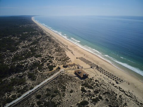 Aerial view of Praia da Comporta with its expansive sandy beach, dunes, and rows of umbrellas along the Atlantic Ocean in Comporta, Setubal, Portugal.