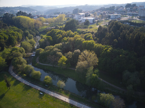 Aerial view of an urban park with a winding river, lush green trees, walking paths, and a town in the background in Portugal.