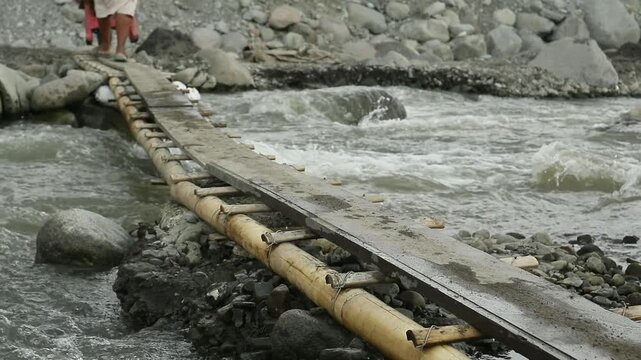 traditional sand mine workers walk on a small bamboo bridge pushing a trolley