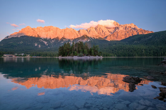 Beautiful sunset glow over the Maximiliansinsel island at Eibsee lake with Zugspitze mountain peaks and rocky foreground in Bavaria, Germany.