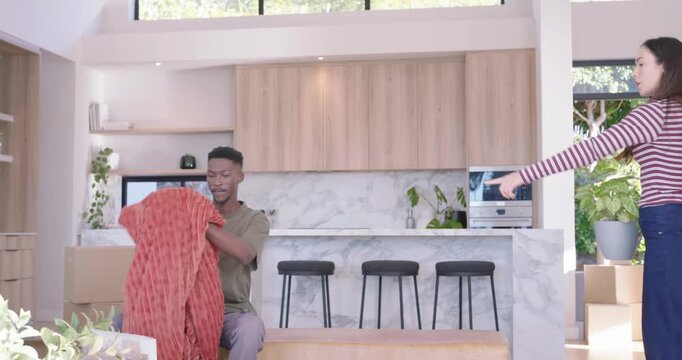 African couple unpacking boxes, placing plant on kitchen island, opening framed art and decorating