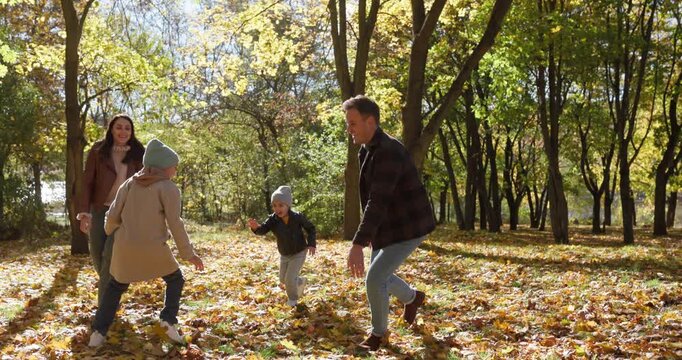 Happy family playing tag in autumn park. Parents and kids laugh, run and toss leaves while walking under yellow fall trees, mother, father and carefree siblings enjoying time outdoors together