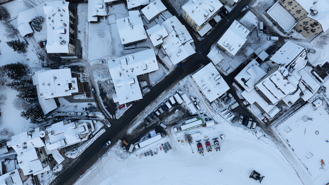 Aerial view of snow-covered rooftops and streets in the mountain village with parked cars and snow grooming equipment Cogne, Aosta Valley, Italy.