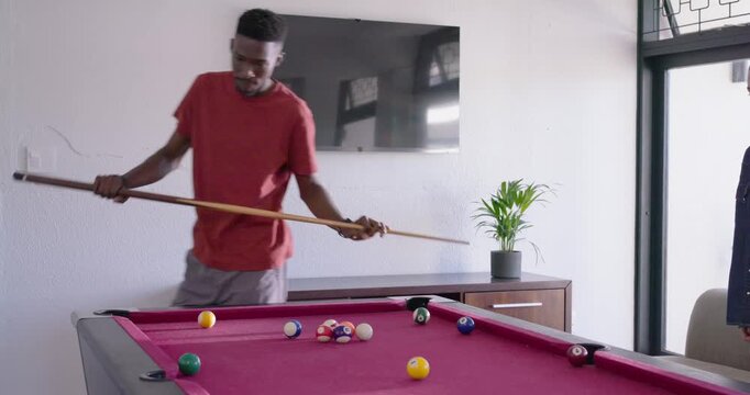 African adult entering frame in game room, inspecting rack, adjusting cue, lining up to break rack