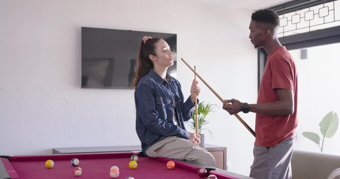 Diverse couple sharing pool tips, man showing cue grip, woman adjusting grip at red-felt pool table