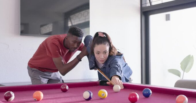 Couple practicing at home pink-felt pool table with man placing arm guiding woman taking cue shot