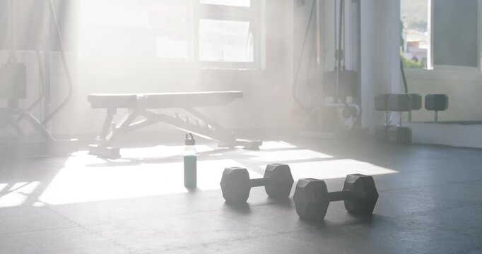 Hex dumbbells are sitting on rubber floor as sunlight is streaming through window, shifting shadows