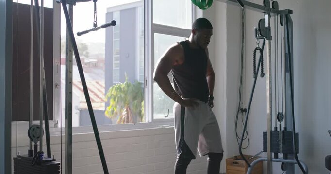 African American man in black tank doing assisted pull-ups in gym, grabbing green band for strength