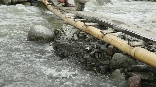 traditional sand mine workers walk on a small bamboo bridge pushing a trolley