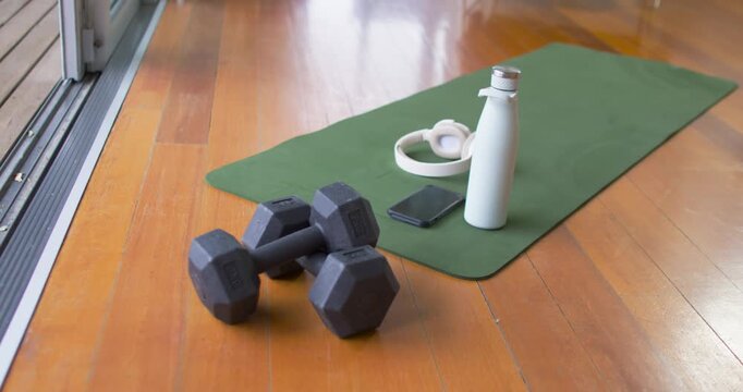 Gentle camera shift is revealing black hex dumbbells, mat and bottle near sliding door for workout