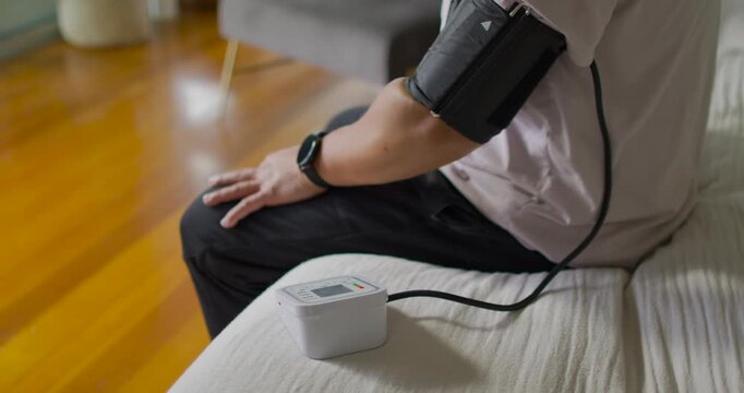 Senior Asian man sitting on sofa cuff inflating, monitor recording blood pressure for health check