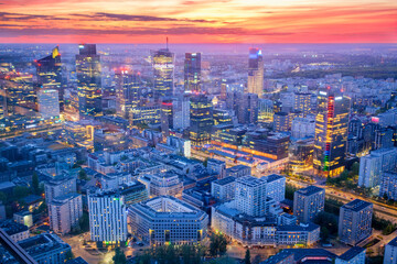 Obraz premium Broad view across the Warsaw skyline in Poland with skyscrapers, city lights, glass high-rises, blue hour twilight and evening glow
