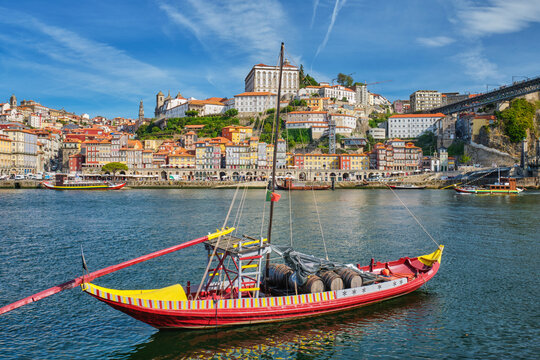 Rabelo boat on the Douro River by Porto Ribeira, Portugal, with wide riverfront skyline and wine barrels near Vila Nova de Gaia