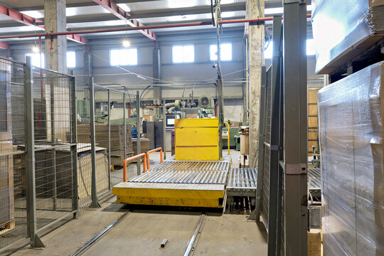 Heavy duty automated transport platform with steel rollers moving on rails inside a modern cardboard manufacturing facility.